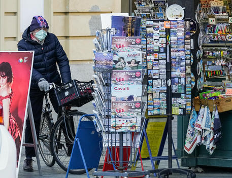 Un uomo con la mascherina in bicicletta davanti ad una edicola a Torino © ANSA