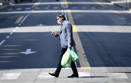 Un uomo cammina in una strada deserta guardando il telefono © ANSA