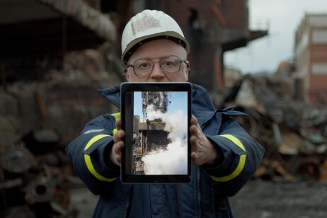 Un operaio nella Ferriera in demolizione tiene in mano un tablet dove scorrono immagini