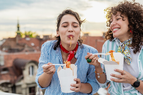 Due donne sorridenti mangiano pasta come street food foto iStock.