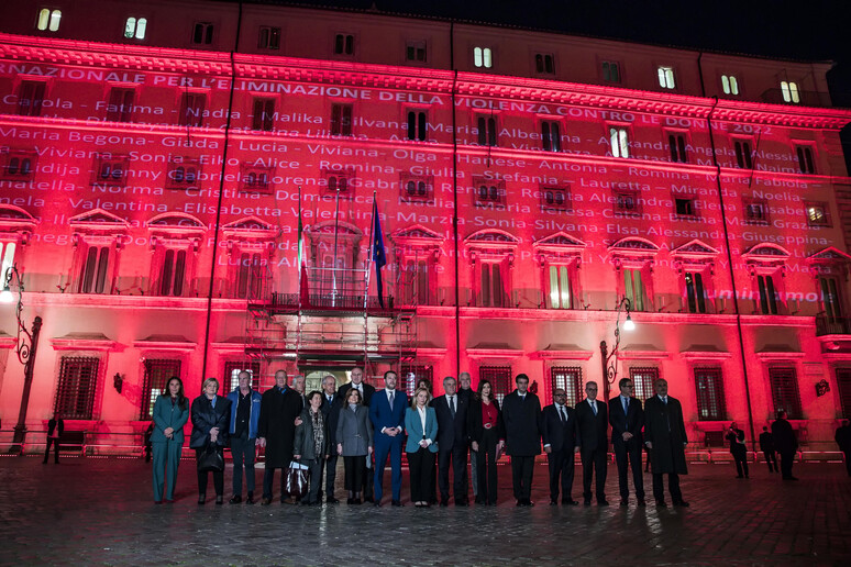 La presidente del Consiglio, Giorgia Meloni, con i ministri davanti a Palazzo Chigi illuminato con luci di colore rosso - RIPRODUZIONE RISERVATA
