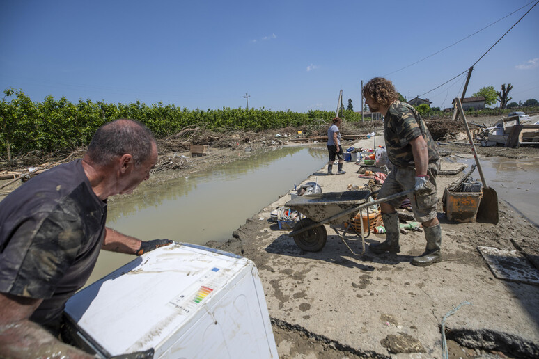 Volontari ripuliscono dal fango una casa alluvionata - RIPRODUZIONE RISERVATA